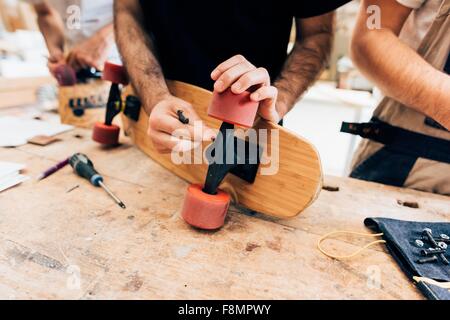 Vista ritagliata di giovani uomini in officina il fissaggio ruote per skateboard Foto Stock