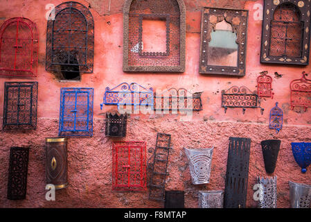 Rivestimento in metallo ganci, lanterne e cornici specchio appeso ad una parete rossa per la vendita nel souk di Marrakech Foto Stock