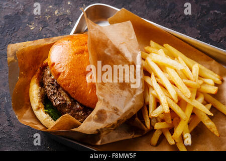 Burger con carne e patate fritte nel vassoio di alluminio su sfondo scuro Foto Stock