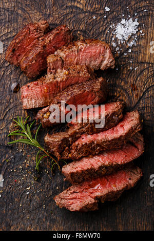 Fette di mezzo raro grigliate di carne di manzo sul tagliere di legno sfondo Foto Stock