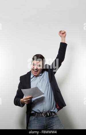 Dai capelli scuri imprenditore europeo ha un momento di pura gioia e tira il suo pugno sinistro in aria mentre si tiene un pezzo di carta in Foto Stock