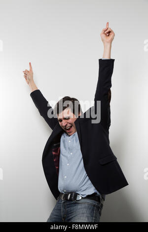 Dai capelli scuri imprenditore europeo si innalza le braccia in una danza di vittoria mentre nella parte anteriore di un gradiente dello sfondo con i suoi occhi clos Foto Stock