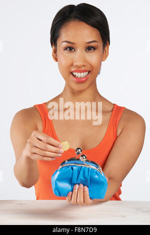 Donna sorridente mettendo Coin in borsa Foto Stock