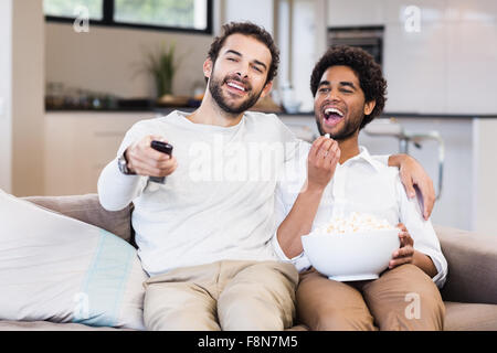 Felice coppia gay guardando la tv mangiare popcorn Foto Stock