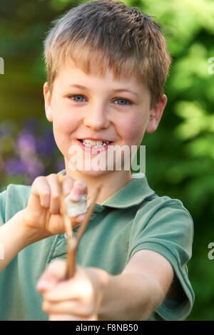 Ragazzo puntando Slingshot in giardino Foto Stock