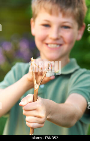 Ragazzo puntando Slingshot in giardino Foto Stock