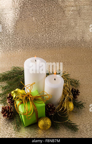La masterizzazione di bianco Natale candele, green box regalo, palline dorate, rami di abete e coni su fondo oro, verticale, spazio di copia Foto Stock