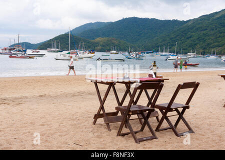 Vuoto con sedie in legno e tabelle in attesa di clienti sulla spiaggia sabbiosa, Vila do Abraao, Ilha Grande Angra dos Reis, Stato di Rio de Janeiro, Brasile Foto Stock