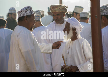 Tre uomini chat della vivace giovedì mercato del bestiame in Nizwa, Oman Foto Stock