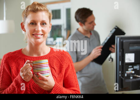 Donna che mantiene la tazza mentre Engineer installa EQUIPAGGIAMENTO TV Foto Stock