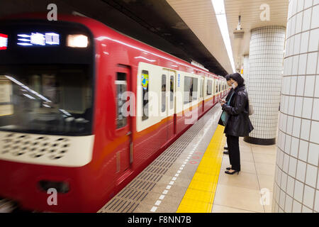 Una donna giapponese in attesa in metropolitana per il passaggio di un treno Foto Stock