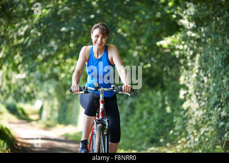 Donna di mezza età ciclismo su strada di campagna Foto Stock