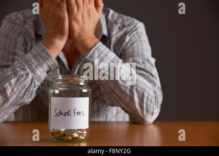Uomo con testa in mani guardando il flacone etichettato tasse scolastiche Foto Stock