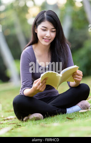 Giovane donna seduta nella lettura del parco Foto Stock