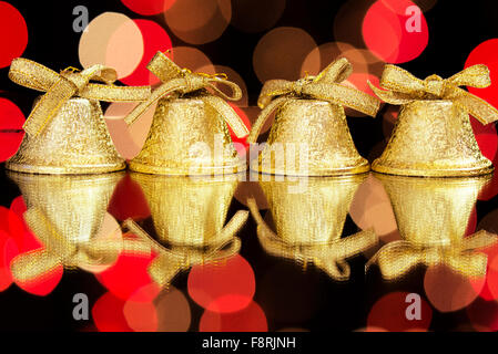 Quattro campane dorate su uno specchio di fronte a uno sfondo nero come una decorazione di Natale Foto Stock