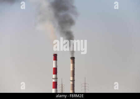 Due inquinanti camini industriali e due pali elettrici contro un cielo chiaro Foto Stock