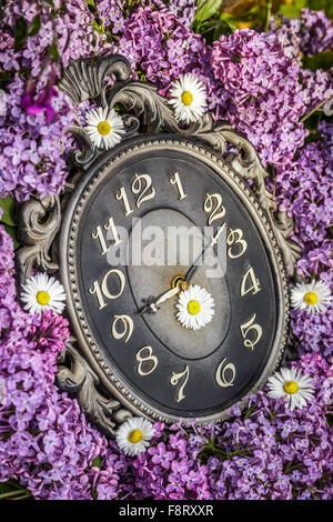 Orologio circondato da fiori di primavera. Profondità di campo con il fuoco selettivo su clock. Fiori lilla Foto Stock