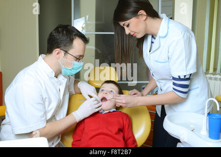 Little Boy in un maglione rosso è andato al dentista nel riunito dentale si siede accanto a un medico per fare il dentista per vedere se i suoi denti Foto Stock