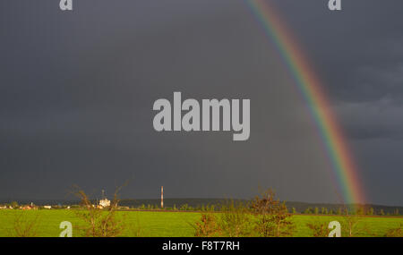 Il drammatico rainbow contro le nuvole scure e il colore insolito del sole Foto Stock