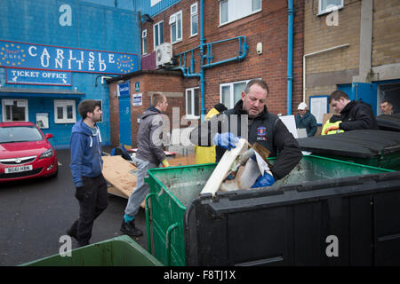 Un volontario di compensazione merci danneggiate dagli uffici a Brunton Park, casa di Carlisle United Football Club in seguito alle inondazioni presso lo stadio. Registrare pioggia caduta in Cumbria hanno causato allagamenti a diverse aree di Carlisle, causando delle case per essere evacuati dai servizi di emergenza. Foto Stock