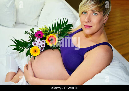 Donna incinta con twin bambinos holding bouquet di fiori Foto Stock