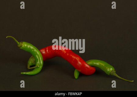 Rosso e peperoncini verdi con gli steli che collegano tra di loro su un sfondo nero Foto Stock