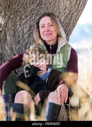 Attraente madre; figlio giovane e piccolo cane posa per fotografie di albero su ranch Foto Stock