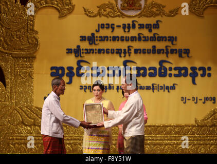 (151212) -- YANGON, Dic 12, 2015 (Xinhua) -- Myanmar Vice Presidente Dott. Sai Mauk Kham (R) anteriore presenta il Premio letterario nazionale per un vincitore letteraria presso il Teatro Nazionale di Yangon, Myanmar, Dic 12, 2015. Complessivamente 18 letterati nazionale ha vinto premi letterari (NLA) per 2014 in Myanmar, il Premio Letterario Nazionale comitato di controllo ha annunciato il Sabato. (Xinhua/U Aung) Foto Stock