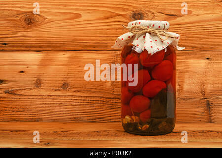 Un grande vaso di vetro di casalinga pomodori sott'aceto con linea tessile decorazione superiore al marrone vintage superficie in legno Foto Stock
