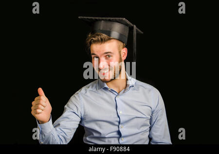 Felice giovane laureato presso il college, con graduazione hat, facendo del pollice in alto segno Foto Stock