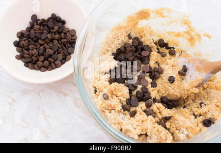 Aggiunta di scaglie di cioccolato al burro di arachidi pasta biscotto in una ciotola di vetro Foto Stock