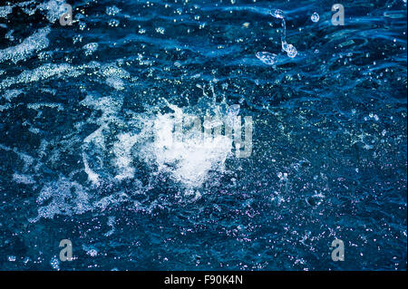Gli spruzzi di acqua e di goccioline incidono blu scuro superficie di acqua in bianco e gli spruzzi di schiuma. Foto Stock