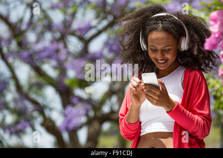 Un attraente mixed-gara giovane donna di parlare o ascoltare la musica sul suo smartphone in un parco all'aperto ubicazione Foto Stock