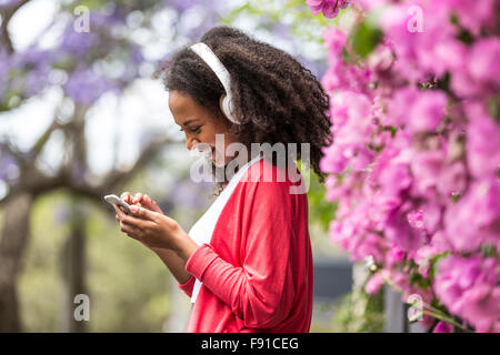 Un attraente mixed-gara giovane donna di parlare o ascoltare la musica sul suo smartphone in un parco all'aperto ubicazione Foto Stock