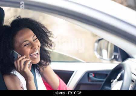 Un attraente razza mista giovane donna in una vettura in chat sul suo telefono cellulare come un passeggero Foto Stock