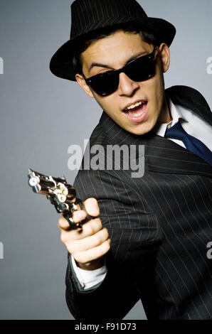 Giovane uomo nel classico costume a strisce tenendo la pistola isolato su grigio Foto Stock