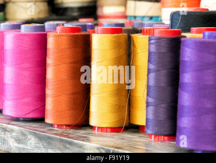 Prodotti tessili ancora in vita - Close Up di taglia industriale rocchetti di filo di cotone in colori vibranti di rosa, arancione, giallo e viola Foto Stock