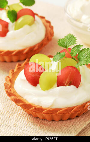 Piccole torte di crema e rabboccato con uve fresche Foto Stock