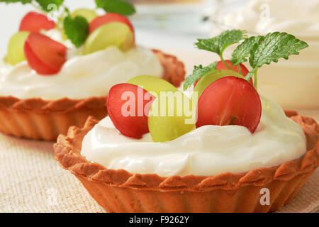 Piccole torte di crema e rabboccato con uve fresche Foto Stock