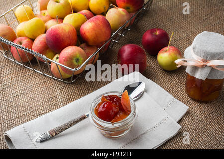 Il vasetto di vetro di marmellata di apple, biancheria igienico e mele in filo metallico cesto su una tela coperti da tavola. Messa a fuoco selettiva. La tonin Foto Stock