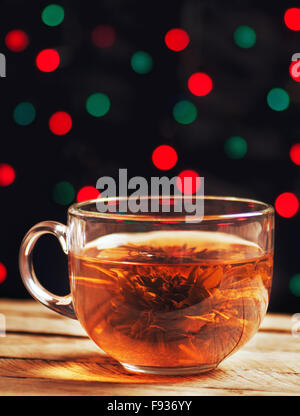 Bicchiere di vetro del tè verde con fiore su un tavolo di legno su un sfondo bokeh di fondo Foto Stock