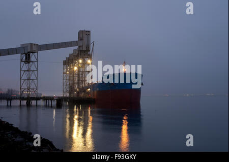 Terminale di granella all'alba nella nebbia con tanker off granella di caricamento Foto Stock