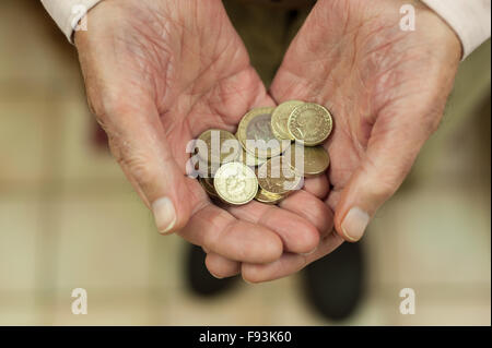 Oro luccicante pound monete trattenute in mani che mostra tutti i piccoli risparmi e motivo di denaro per aiutare colpiti dalla povertà titolare di pensione o di rendita Foto Stock