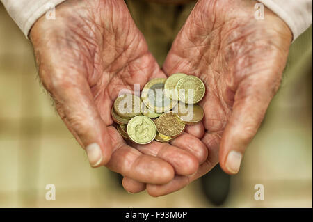 Oro luccicante pound monete trattenute in mani che mostra tutti i piccoli risparmi e motivo di denaro per aiutare colpiti dalla povertà titolare di pensione o di rendita Foto Stock