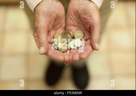 Oro luccicante pound monete trattenute in mani che mostra tutti i piccoli risparmi e motivo di denaro per aiutare colpiti dalla povertà titolare di pensione o di rendita Foto Stock
