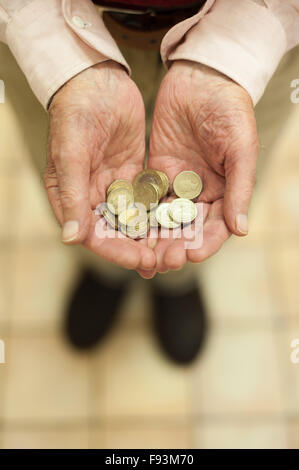 Oro luccicante pound monete trattenute in mani che mostra tutti i piccoli risparmi e motivo di denaro per aiutare colpiti dalla povertà titolare di pensione o di rendita Foto Stock