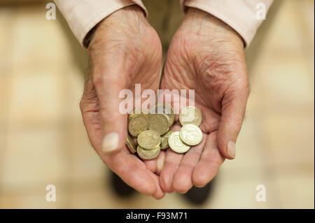 Oro luccicante pound monete trattenute in mani che mostra tutti i piccoli risparmi e motivo di denaro per aiutare colpiti dalla povertà titolare di pensione o di rendita Foto Stock