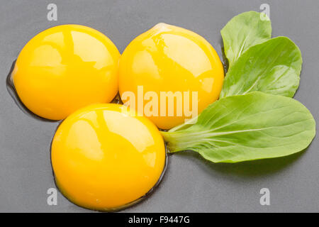 3 tuorlo d'uovo su nero con foglie di colore verde Foto Stock