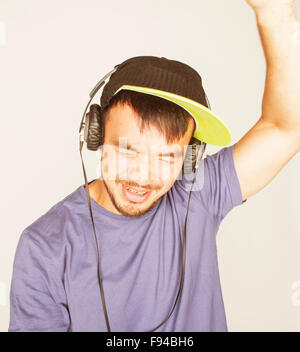 Giovane uomo asiatico in hat e cuffie ascoltando musica su sfondo bianco Foto Stock