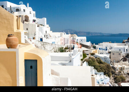 Santorini, Oia. Vista lungo la città, costruita sulla roccia inclinata, con bianche case cubiform e sullo sfondo le scogliere della caldera, il mare e il cielo blu. Foto Stock